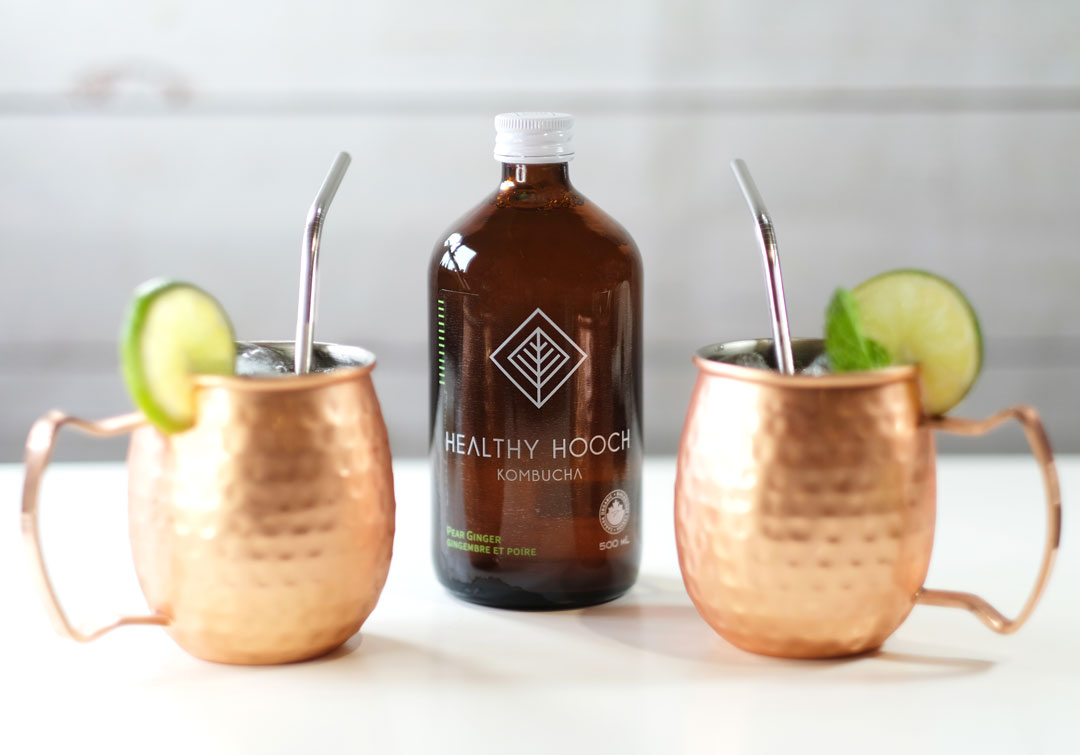 two copper moscow mule glasses with a bottle of healthy hooch