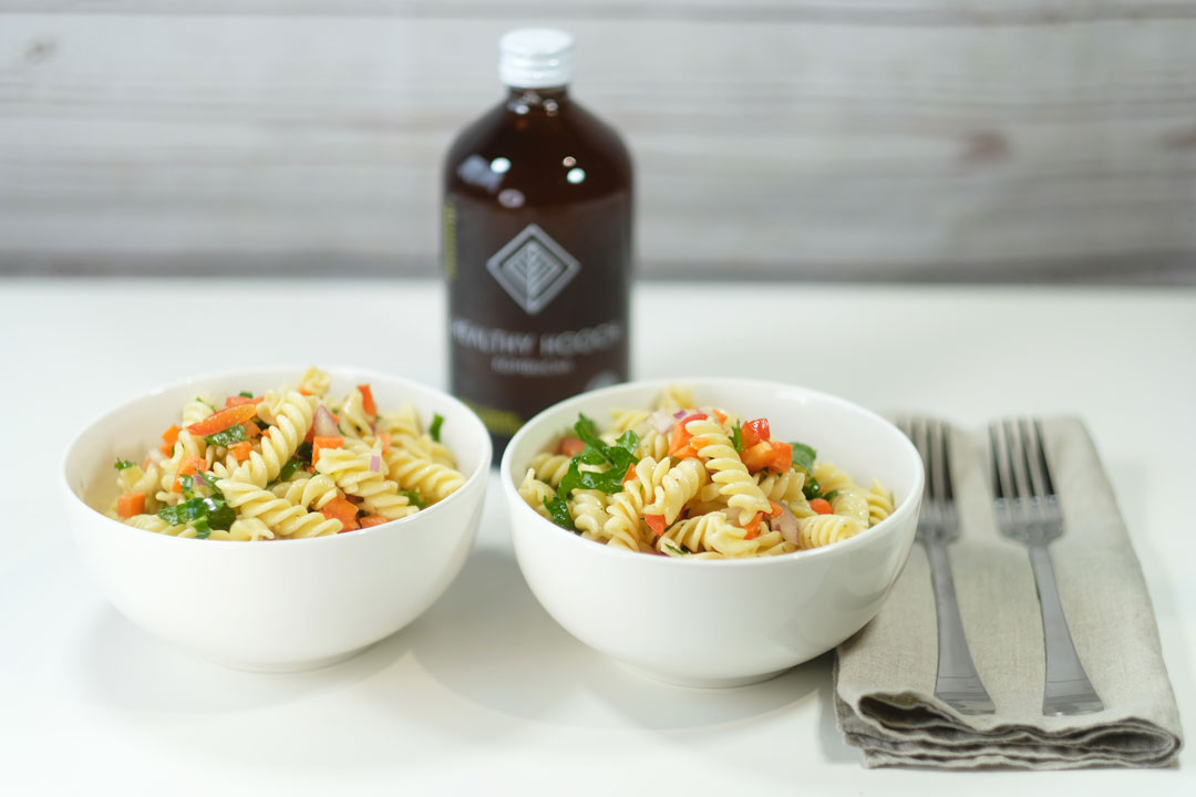 two bowls of pasta salad next to a bottle of kombucha