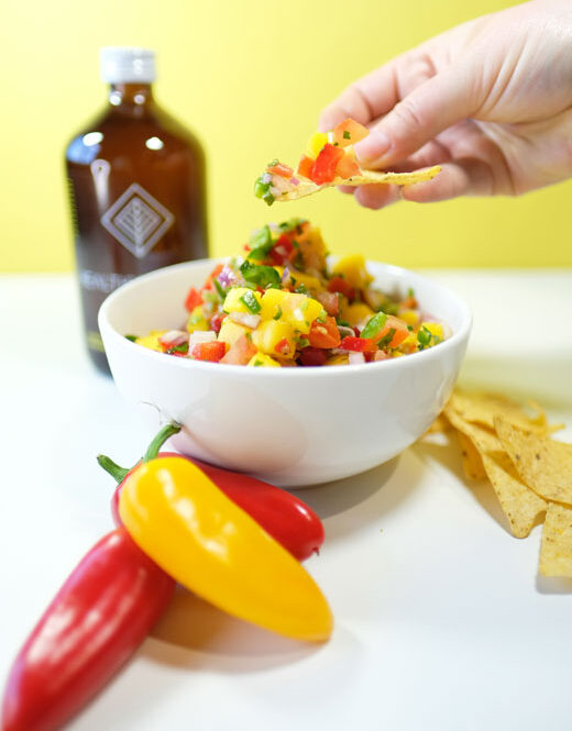 persons hand scooping mango salsa onto a tortilla chip
