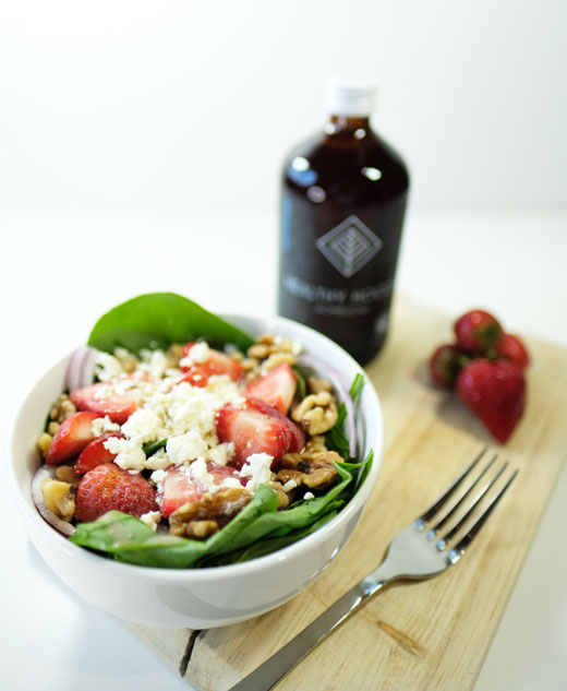 summer salad next to a bottle of healthy hooch kombucha and some berries
